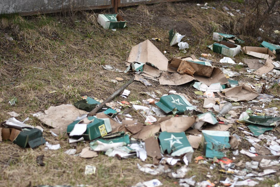 A scene of waste removal featuring a blue skip truck dumping a large quantity of mixed household and commercial rubbish into a waste disposal site. The truck, positioned on the right, has its hydrauli